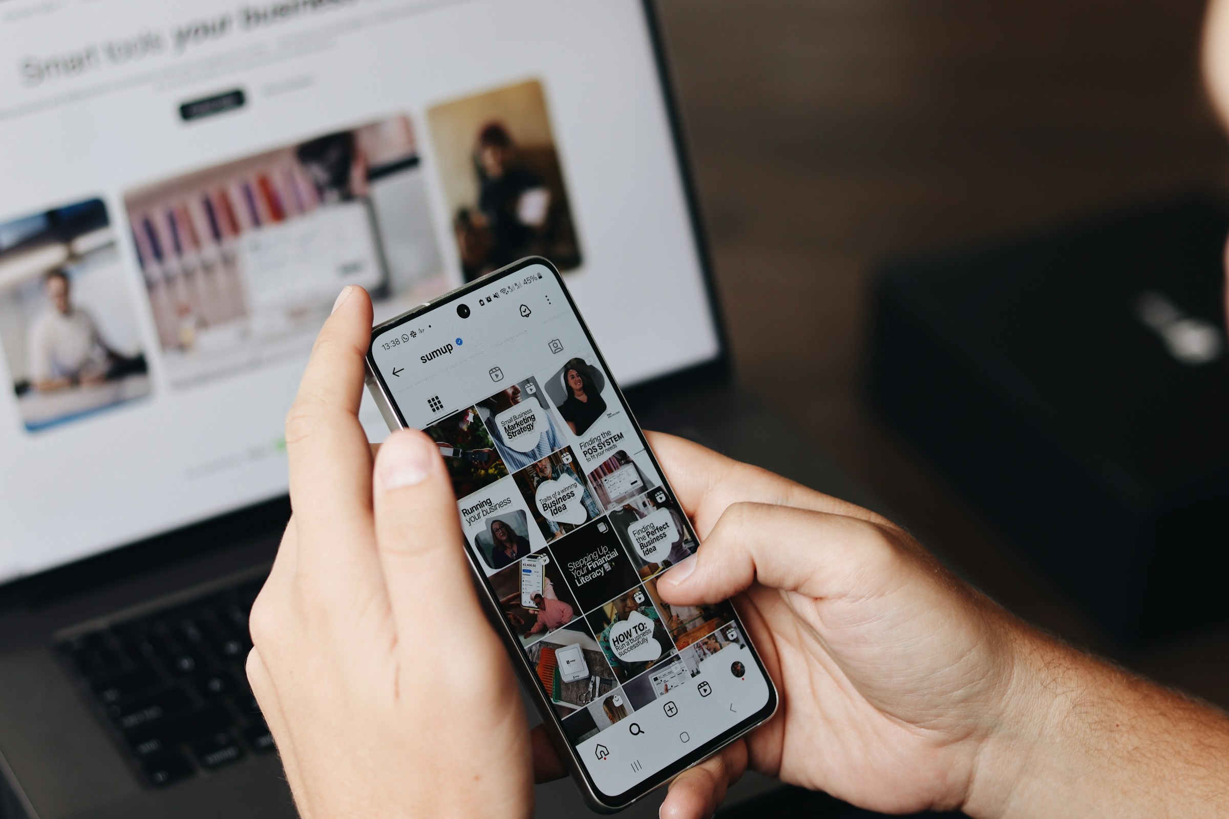 Reviewing an Instagram content feed on a phone beside a laptop